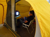Camp Up To Now installation by Ayin Es, exterior tent showing people inside watching movie on little tv